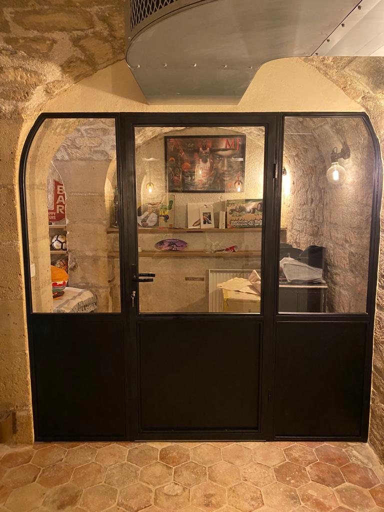 Perete interior vitrat din oțel, cu ușă, într-o încăpere boltită din piatră